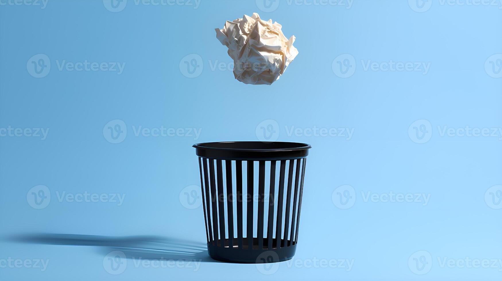 Crumpled paper ball falling into black wastebasket on blue background photo