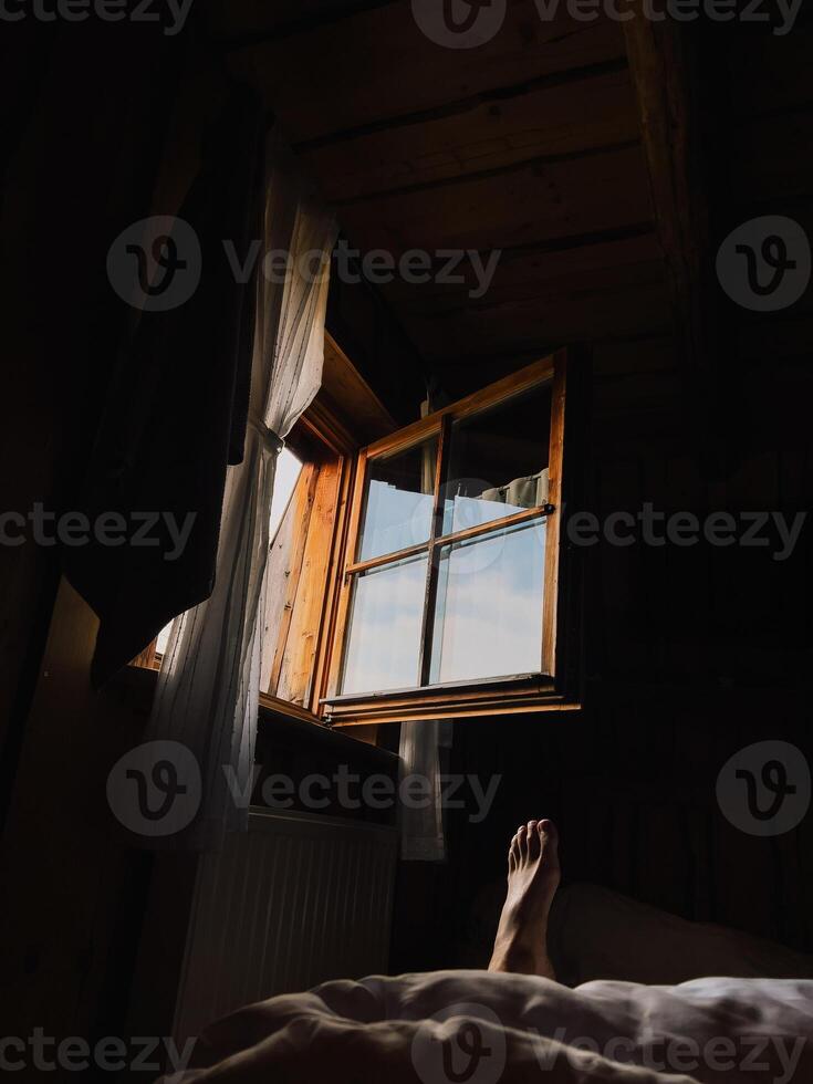 Sunlight streams through an open window in cozy wooden cabin, illuminating foot resting on bed, suggesting peaceful and relaxing morning. Sunlight casting soft glow on relaxed foot resting on bed photo