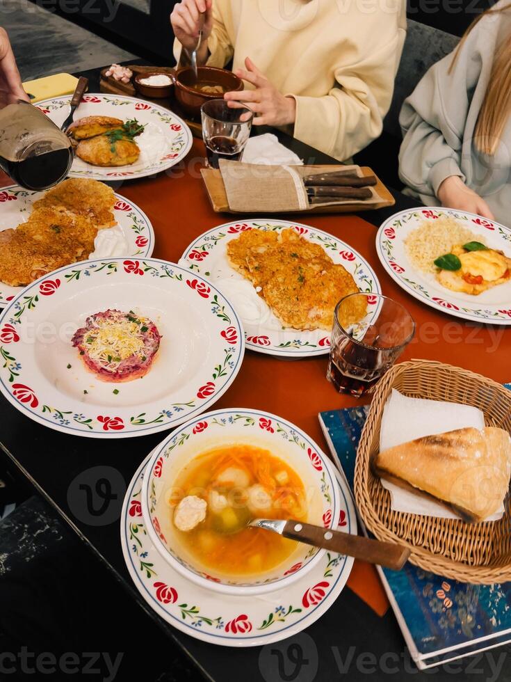 People are sharing a meal of potato pancakes, soup, salad, and bread, served on decorative plates and bowls in a cozy restaurant setting, highlighting the rich culinary traditions of Eastern Europe photo