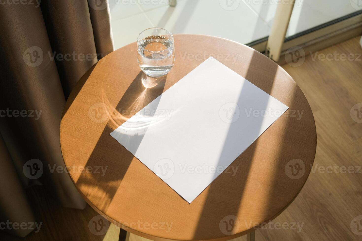 blank paper poster mockup on wooden coffee table with glass of water photo