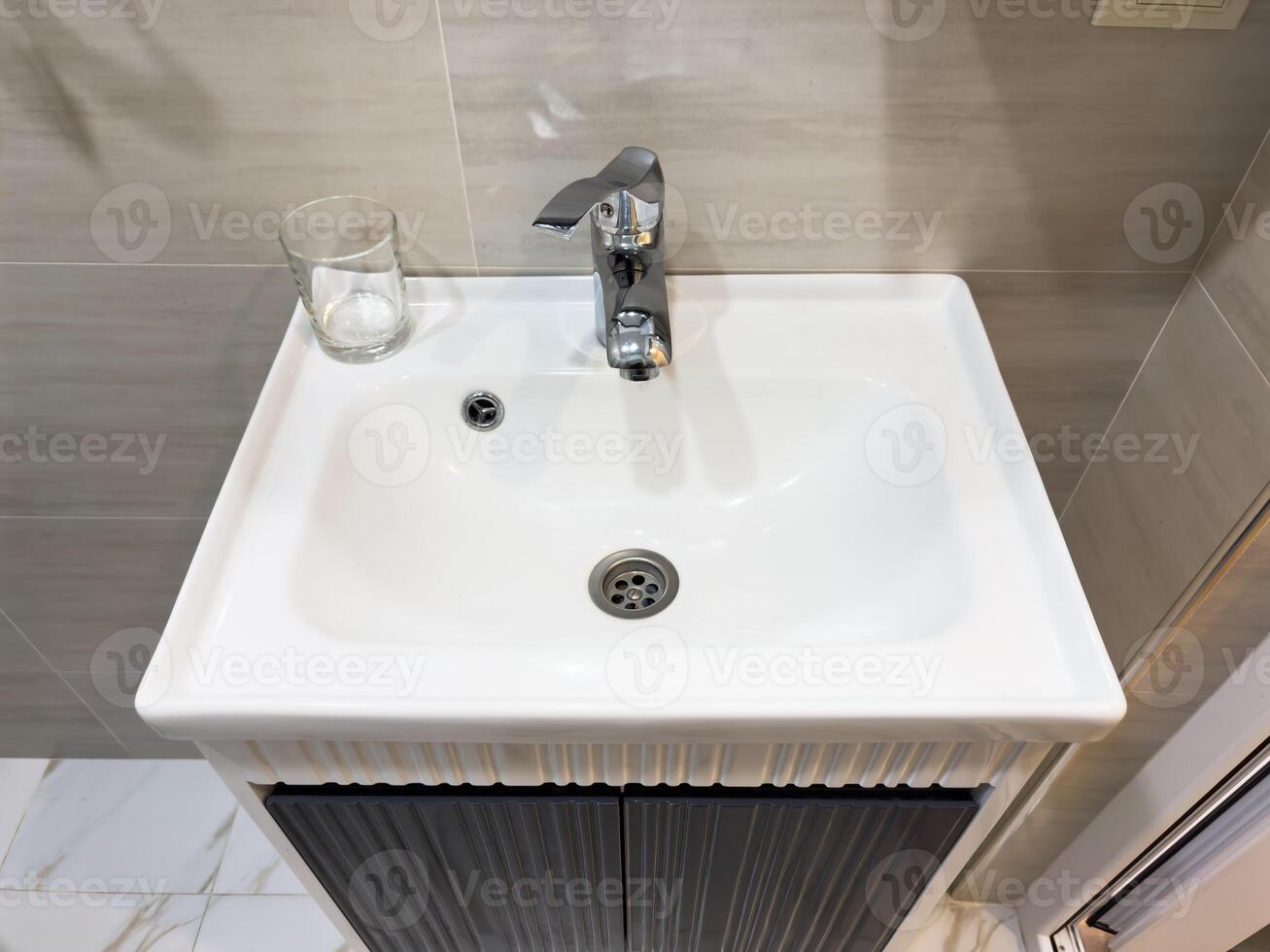 A sink with a silver faucet and a glass on the counter photo