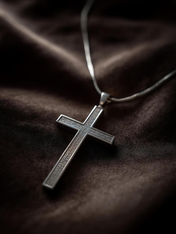 Close up of a silver cross necklace resting on dark fabric. photo