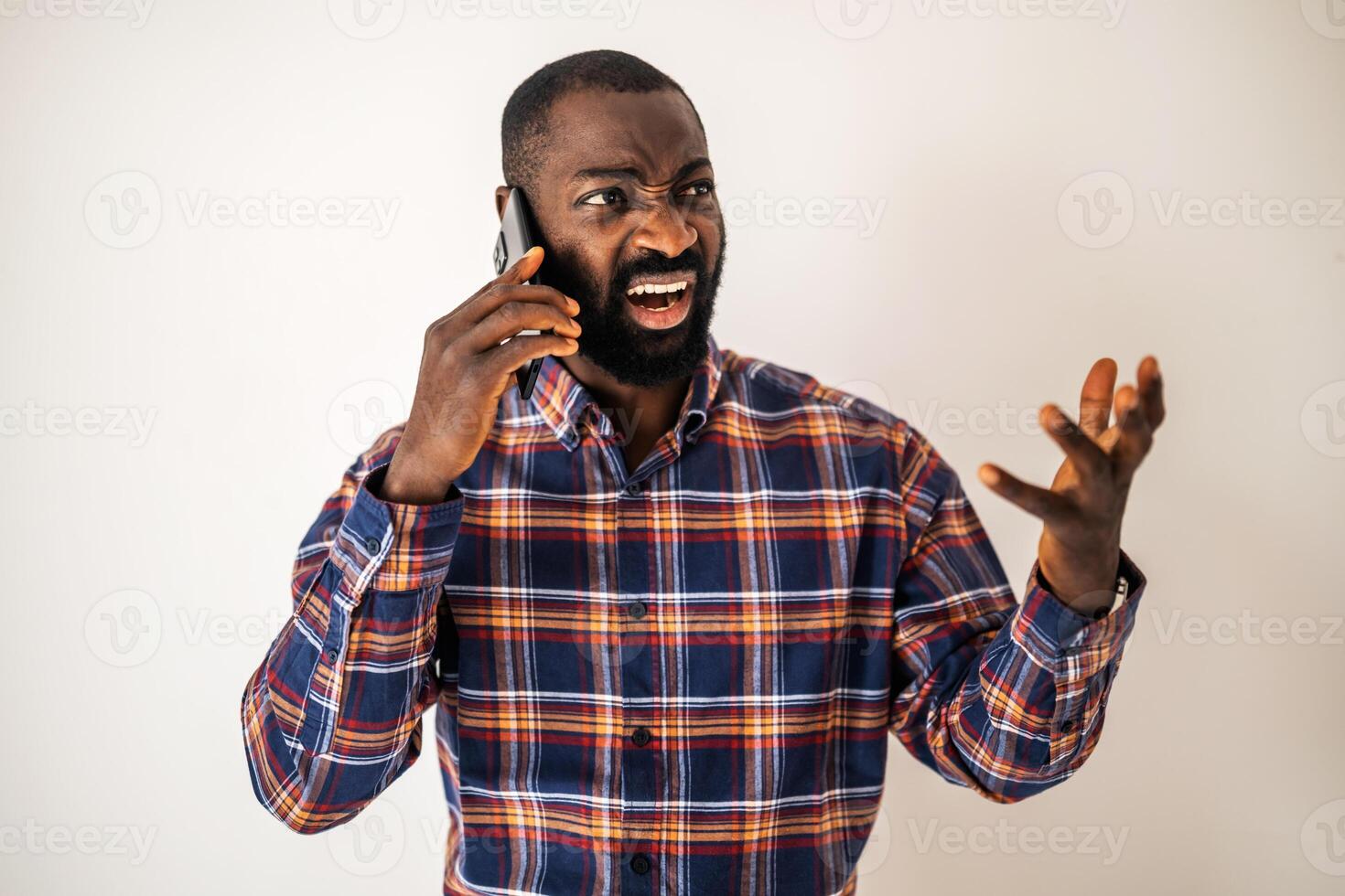 Frustrated African American man with beard shouting while holding mobile phone, showing signs of overwork and emotional strain. photo