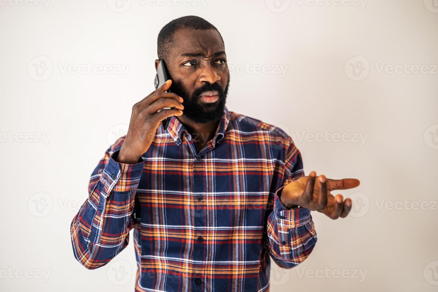 Confused and worried young African American man with a beard, expressing displeasure during a phone conversation. photo