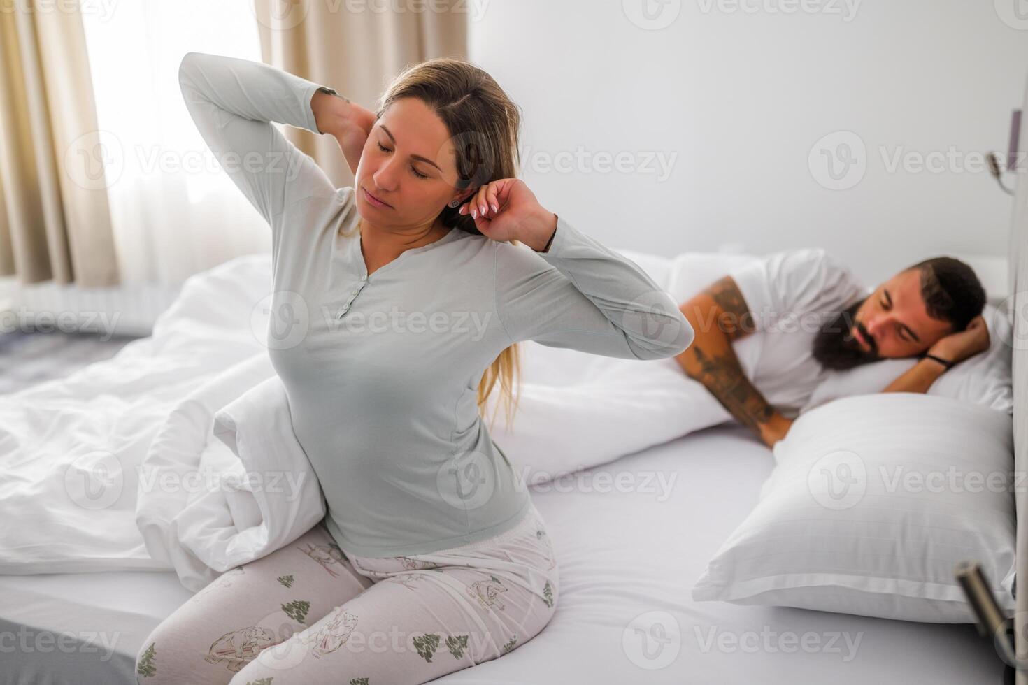 Woman waking up and stretching comfortably in bed, enjoying the calm start of her day, while her husband still sleeping. photo
