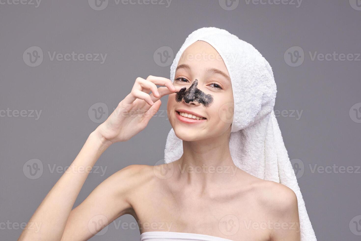 Young caucasian female applying blackhead mask with towel on head smiling skincare routine. photo