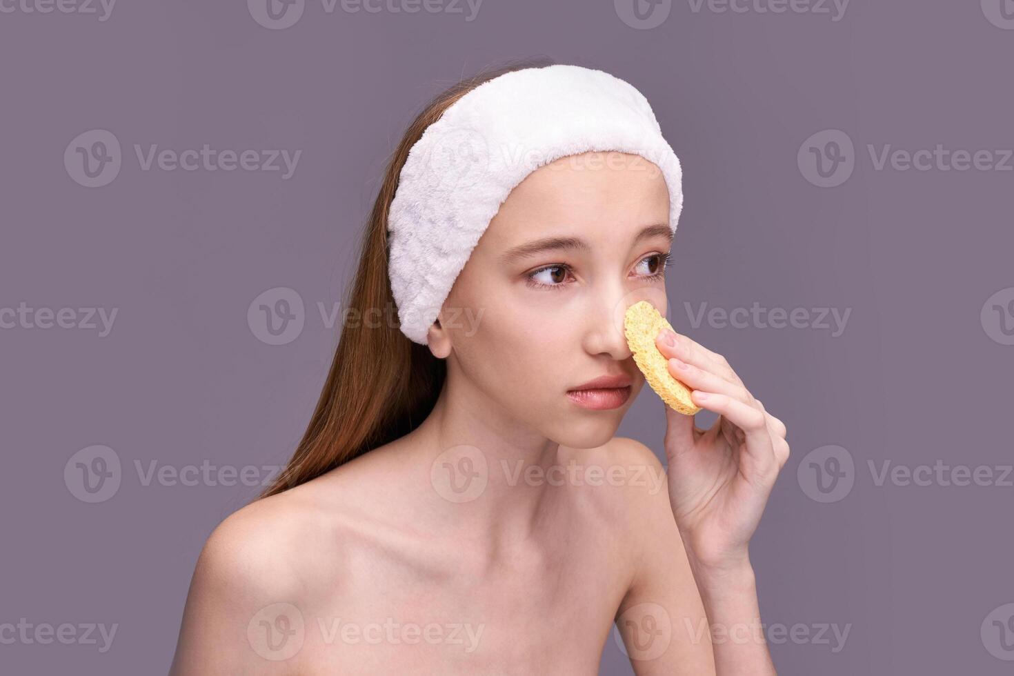 Young caucasian female skincare routine with facial sponge and white headband on neutral background. photo