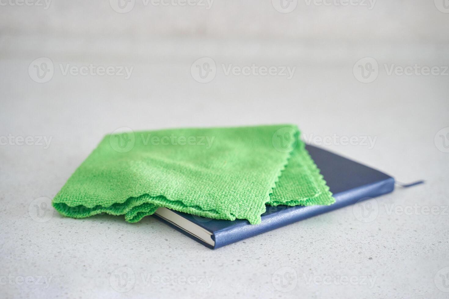 Green cleaning cloth on closed blue notebook on white surface. photo
