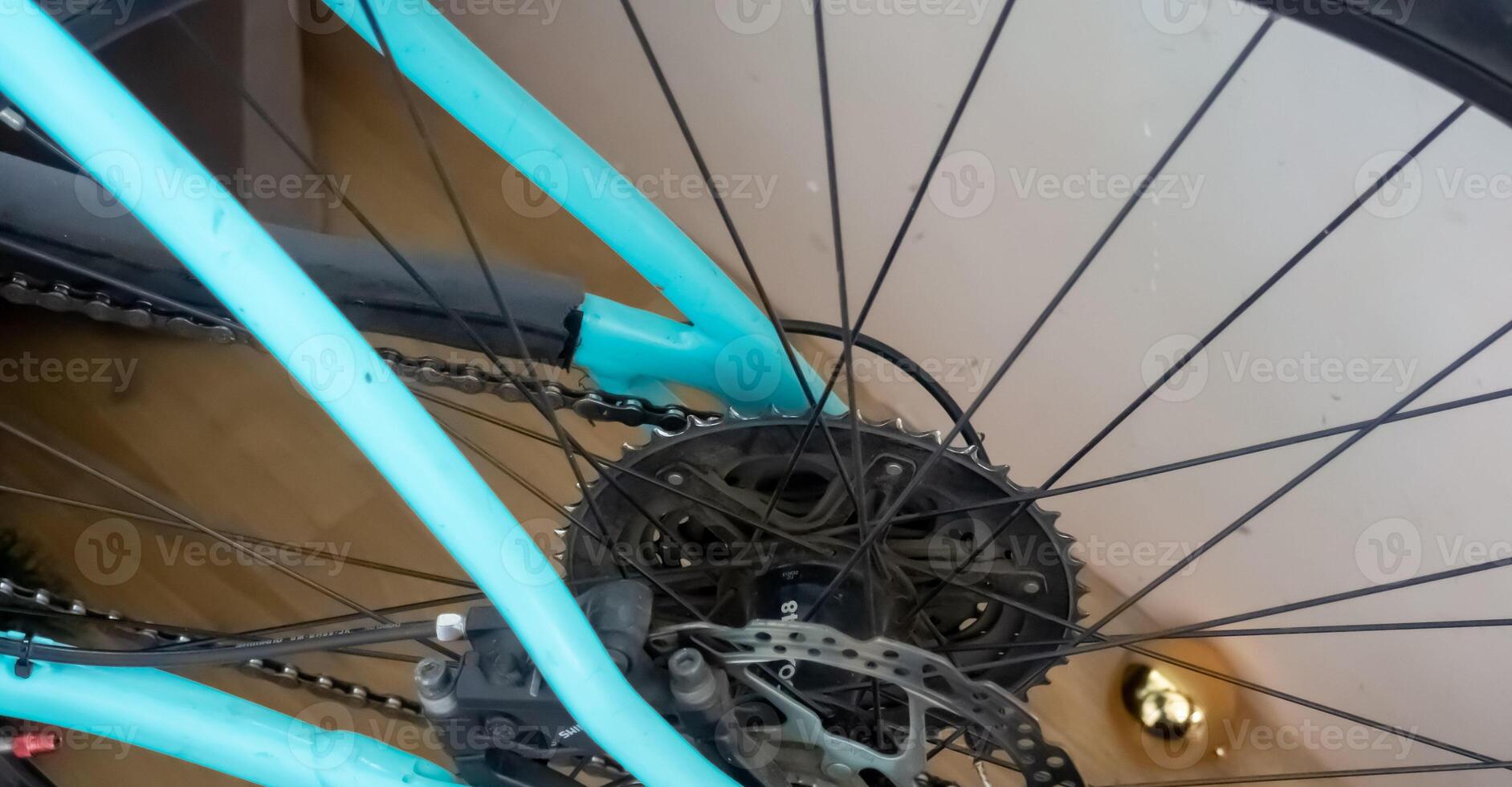 Close-up of a bicycle wheel with a turquoise frame and black spokes. The gear mechanism is visible, showcasing the intricate details of the bike's design. photo