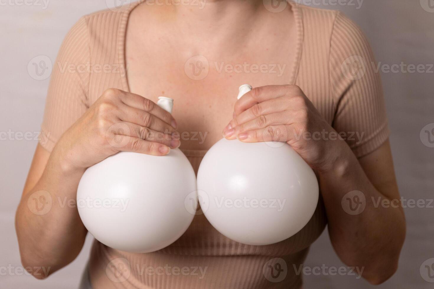 A flesh-colored T-shirt woman stands in front of the camera holding balloons in her hands photo