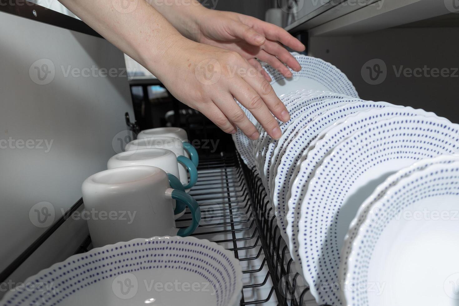 Hands Carefully Arranging Clean Dishes in a Kitchen Drying Rack After Washing photo