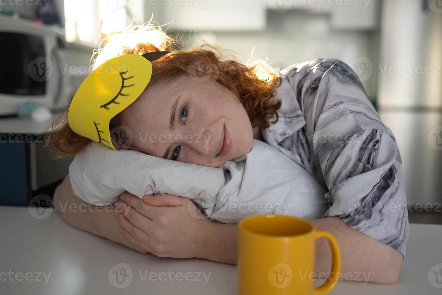 A woman with a sleep mask sits at a table with coffee photo