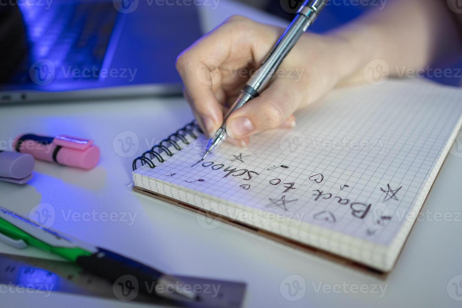 A student's hand writes Back to School in a grid notebook with a pen, surrounded by study supplies, symbolizing education, learning, and academic preparation photo