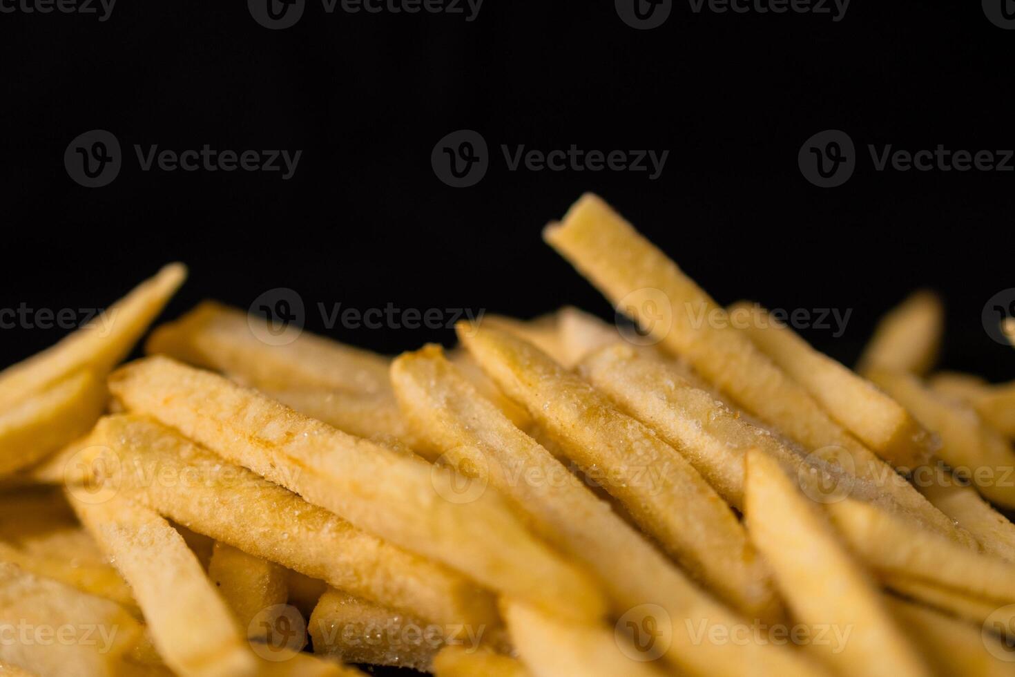 Close-up of raw golden french fries, glistening with seasoning, piled high against a dark background, ready for deep frying, symbolizing popular fast food snack options photo