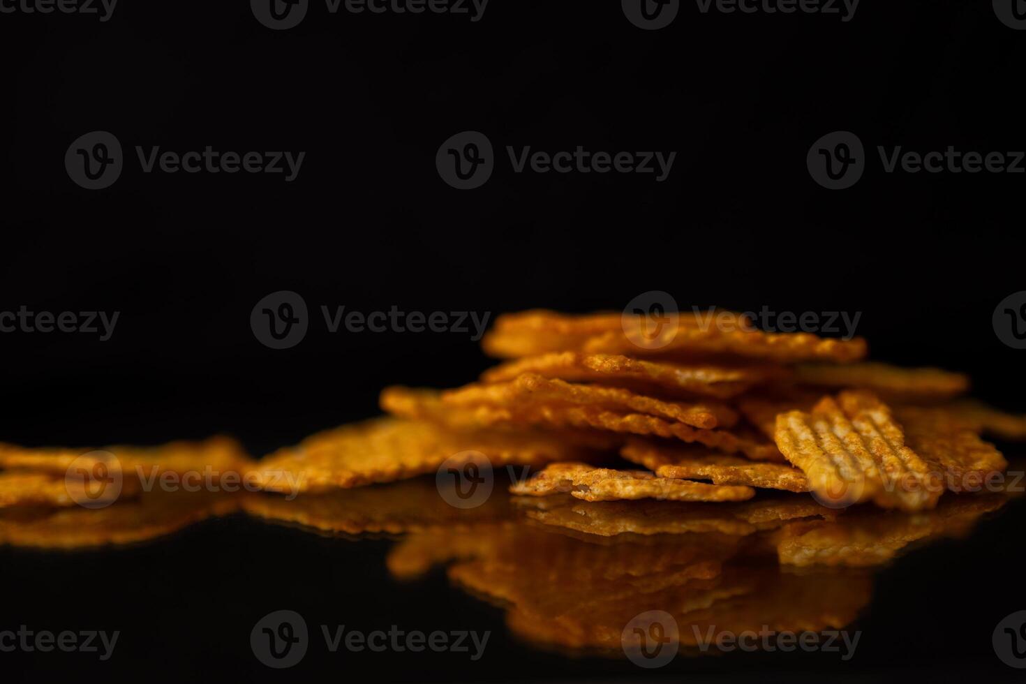 Golden ridged potato chips piled on a dark reflective surface, emphasizing their crispy texture and delicious snack appeal for a quick bite photo