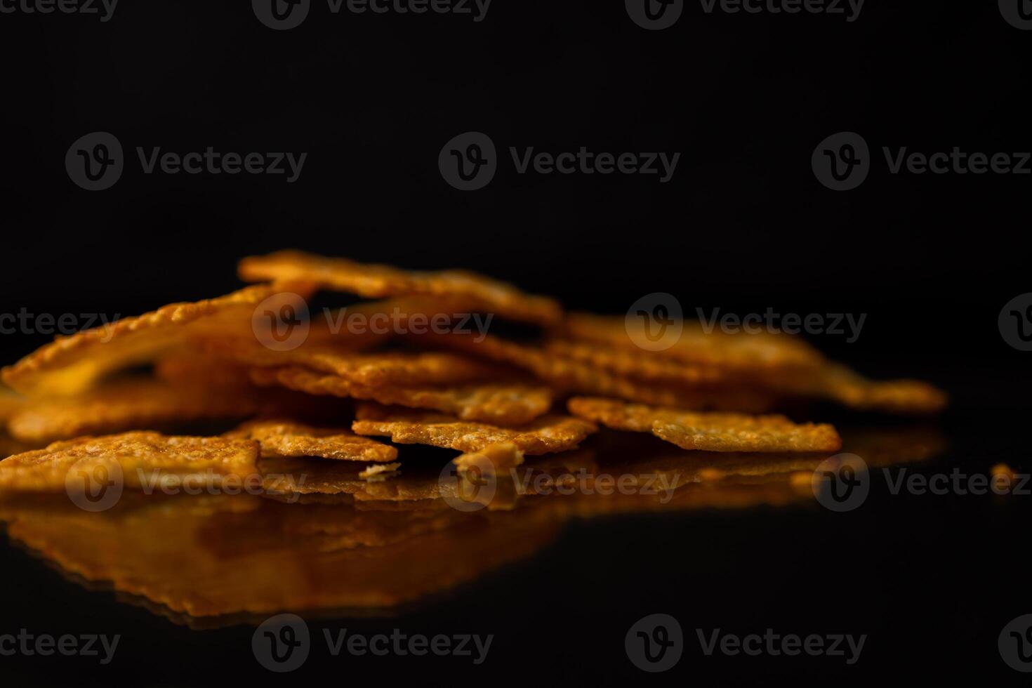 A close-up of delicious golden crackers stacked with a crisp texture, casting a reflection on a sleek dark surface, highlighting savory snack food photo