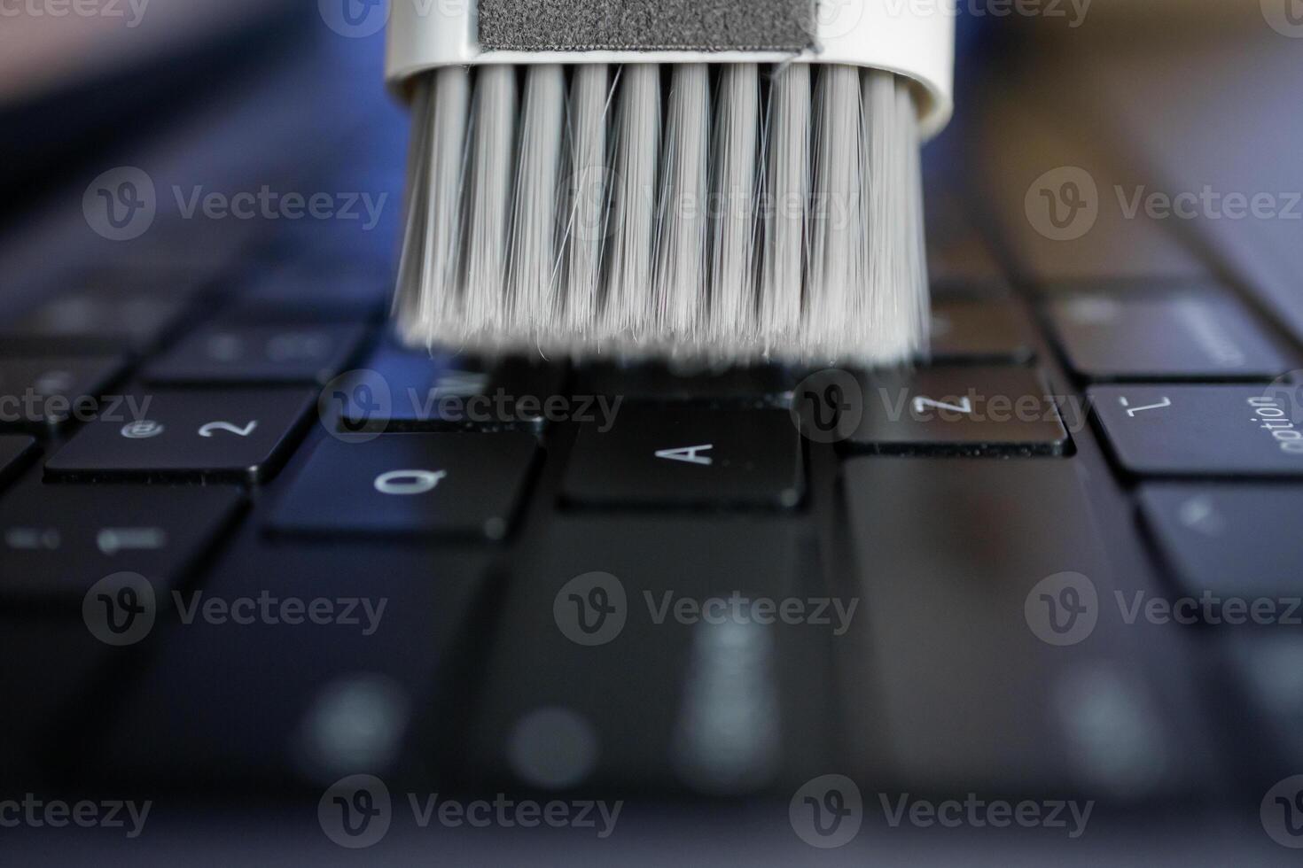 White cleaning brush sweeps dust from a black laptop keyboard, representing essential technology maintenance for optimal productivity and device longevity photo