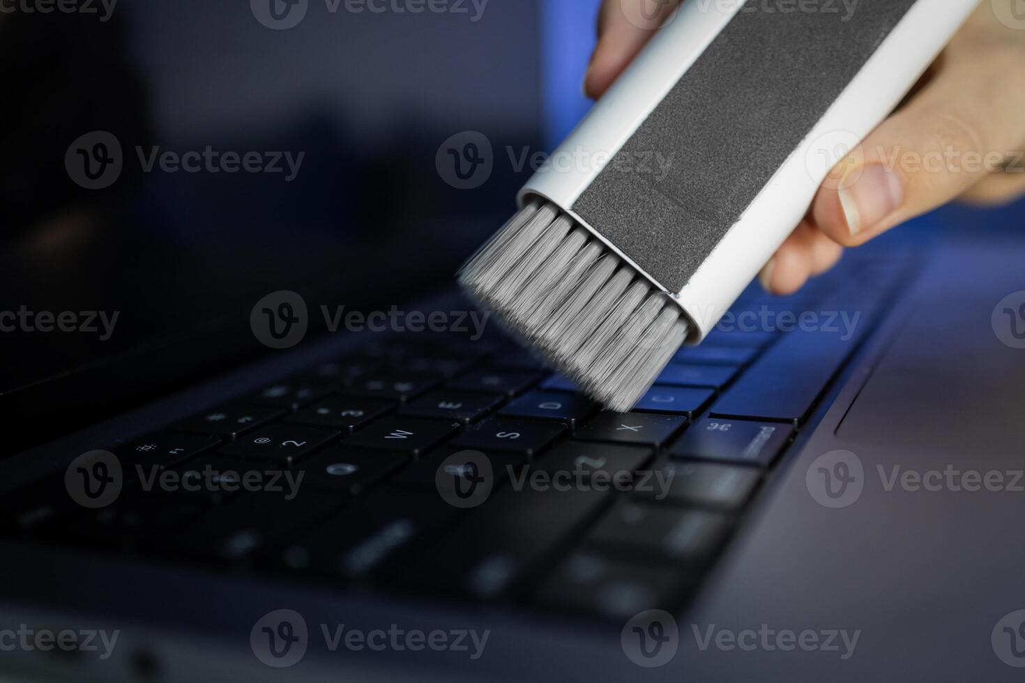 Person's hand cleaning a laptop keyboard with a specialized brush, ensuring thorough device maintenance and promoting a hygienic digital workspace photo