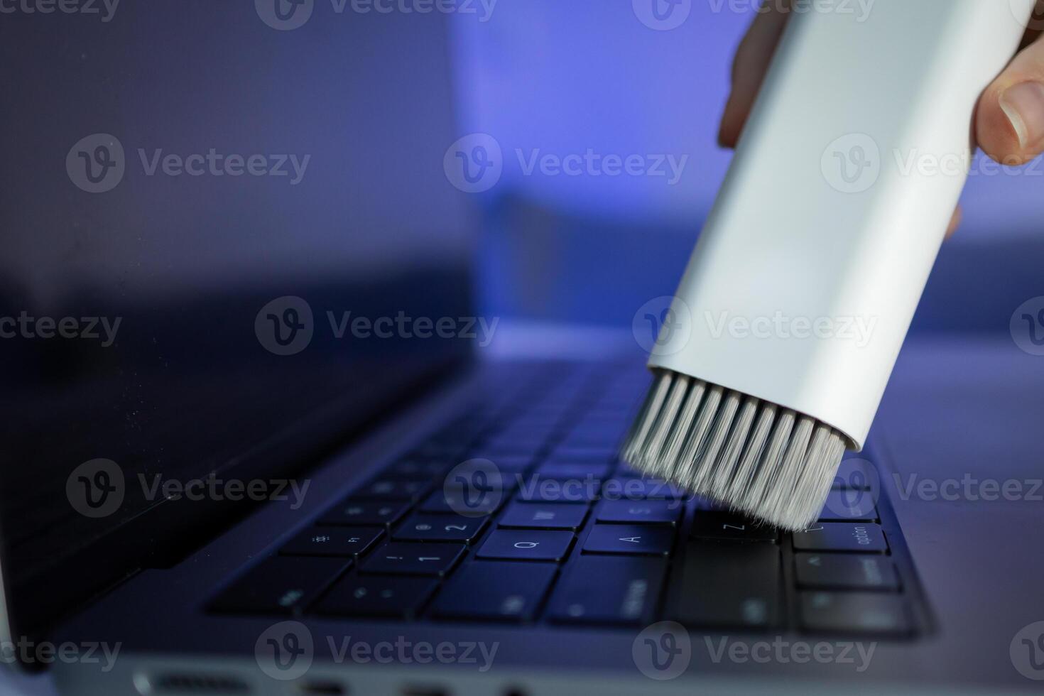 A white cleaning brush diligently sweeps dust off a sleek laptop keyboard, promoting essential electronic device care and regular maintenance for improved longevity photo