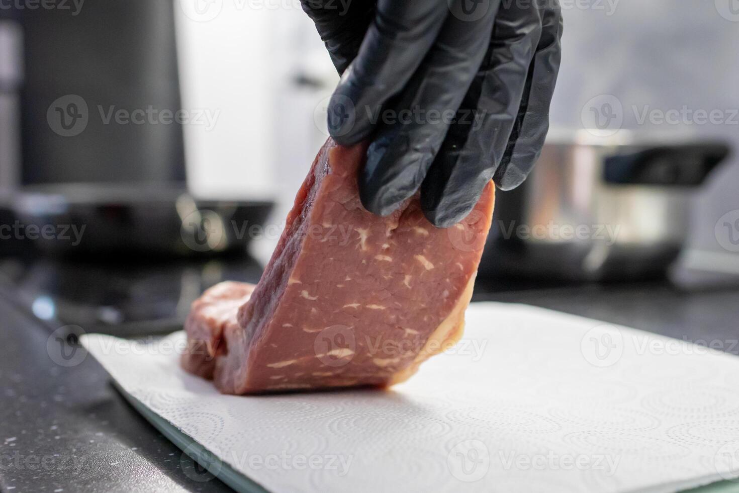 A person in a black glove carefully places a fresh raw beef steak onto a white paper towel, emphasizing hygiene and quality in kitchen food preparation photo