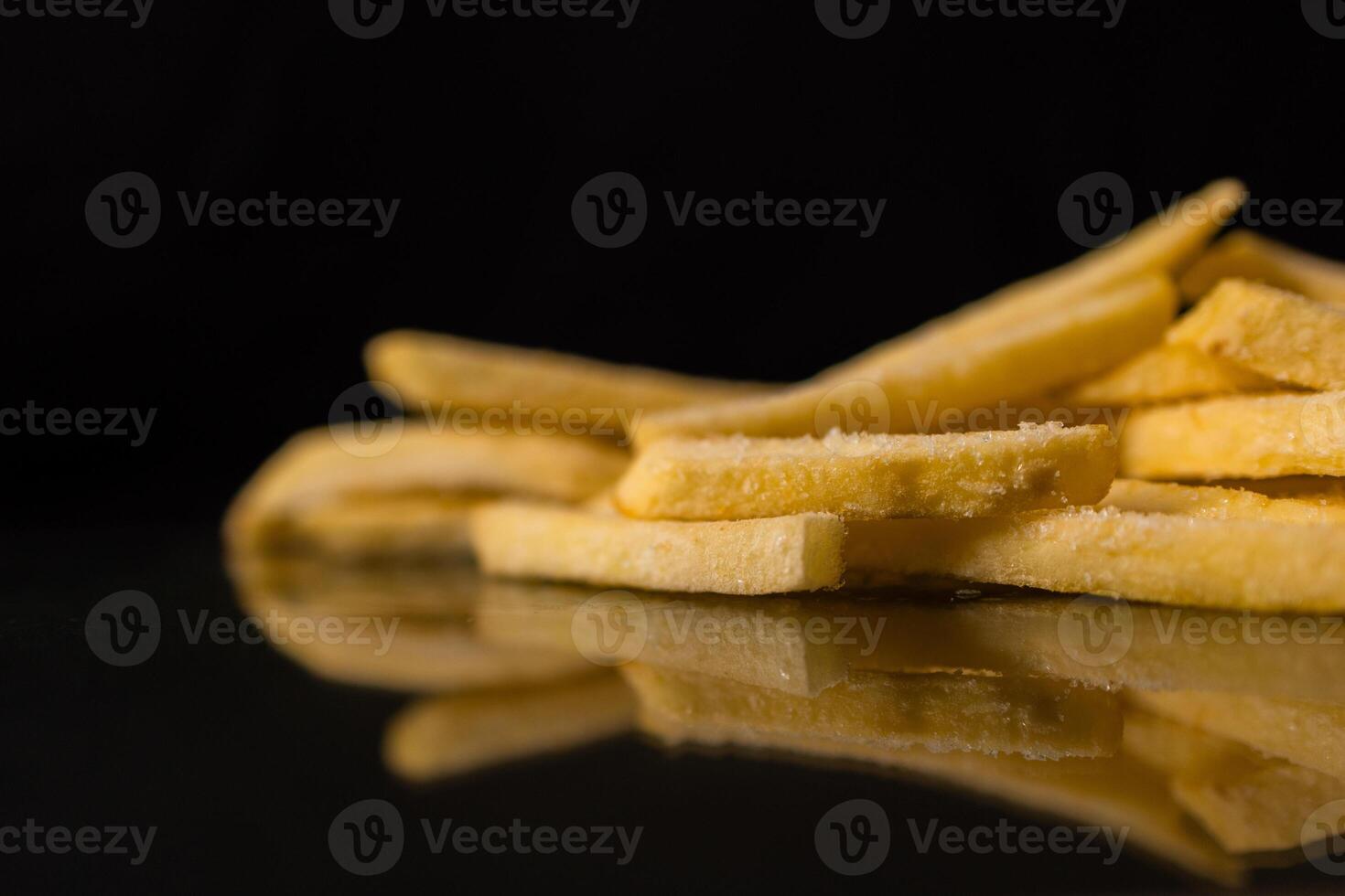 Uncooked golden frozen french fries with visible frost crystals, neatly stacked on a sleek dark reflective surface, highlighting fast food photo