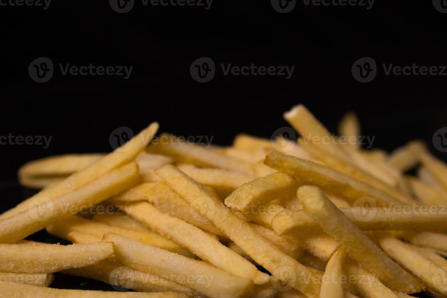 A large pile of uncooked frozen french fries with a frosty surface against a dark background, representing a common fast food item and convenient meal option photo