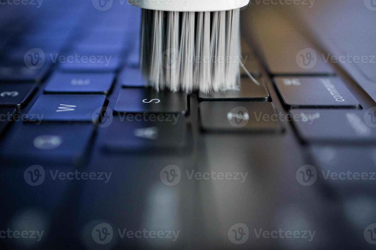 White cleaning brush sweeping across a laptop keyboard, symbolizing essential electronic device maintenance, ensuring longevity and efficient digital workflow for users photo