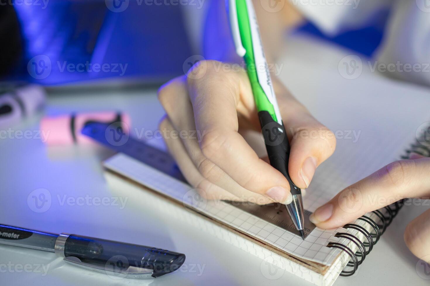 Student's hand diligently using a green pen and ruler on a grid notebook, illustrating academic precision, focused learning, and effective study methods photo
