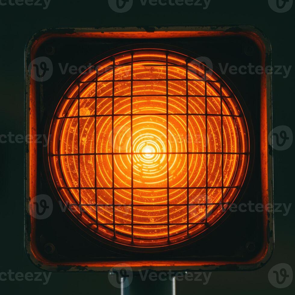 Close up of a bright orange traffic signal light with a protective grid against a dark background photo
