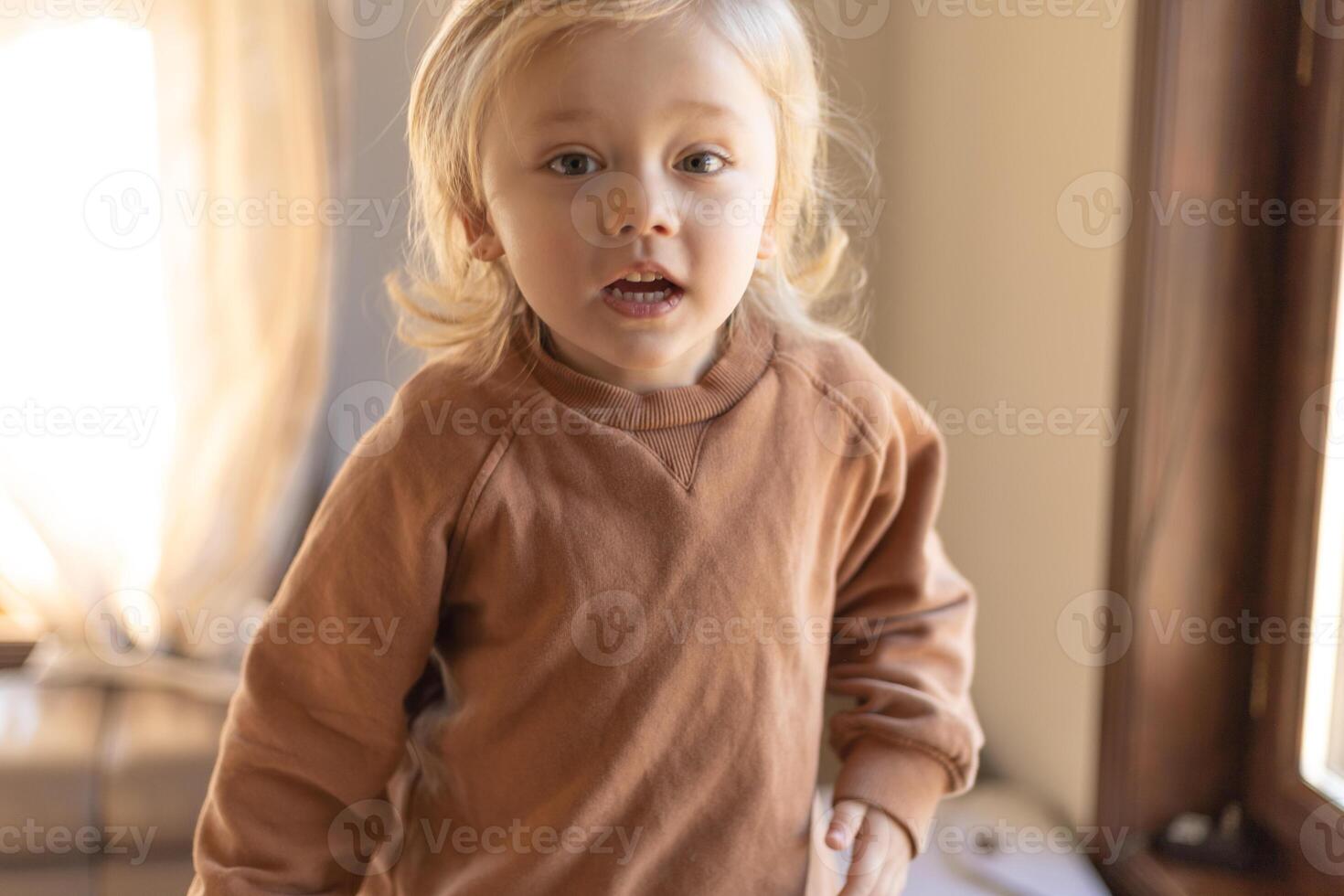 A three-year-old boy with blond curly hair is jumping on the couch at home photo