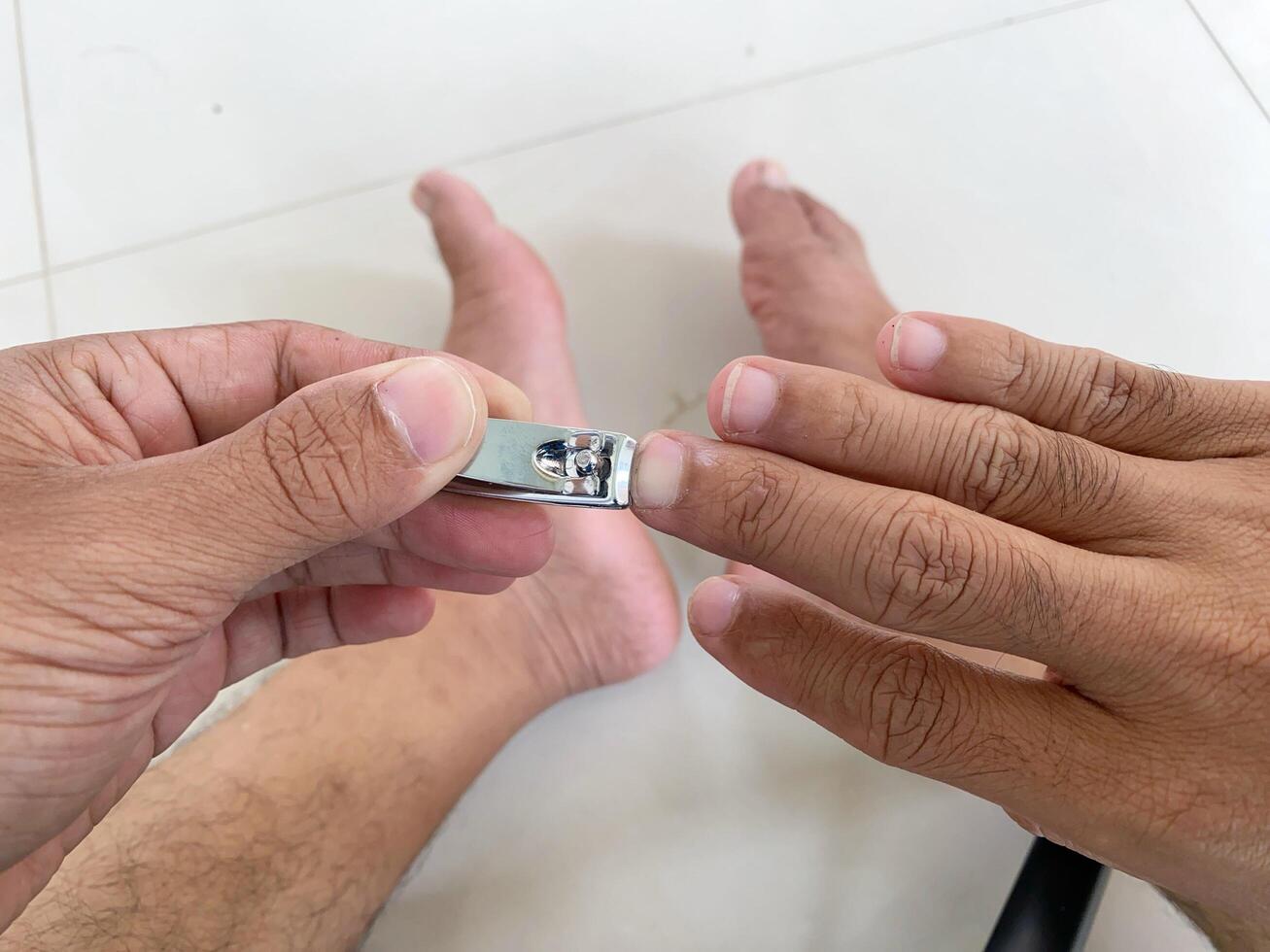 Cutting fingernails with clippers shows personal grooming and self-care at home on white tile. photo