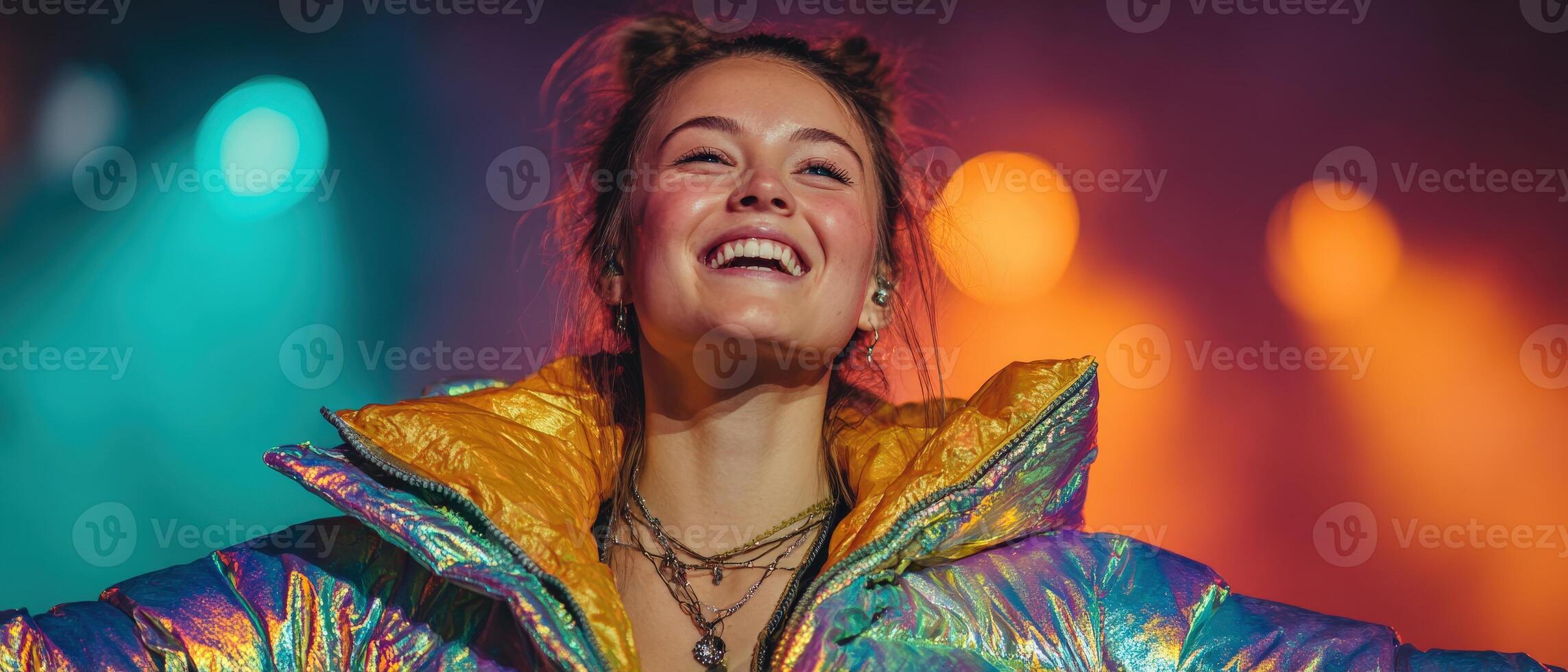 Smiling Caucasian woman in iridescent puffer jacket with layered necklaces, illuminated by vibrant stage lights Concept of music performance, youth culture, and positive energy photo