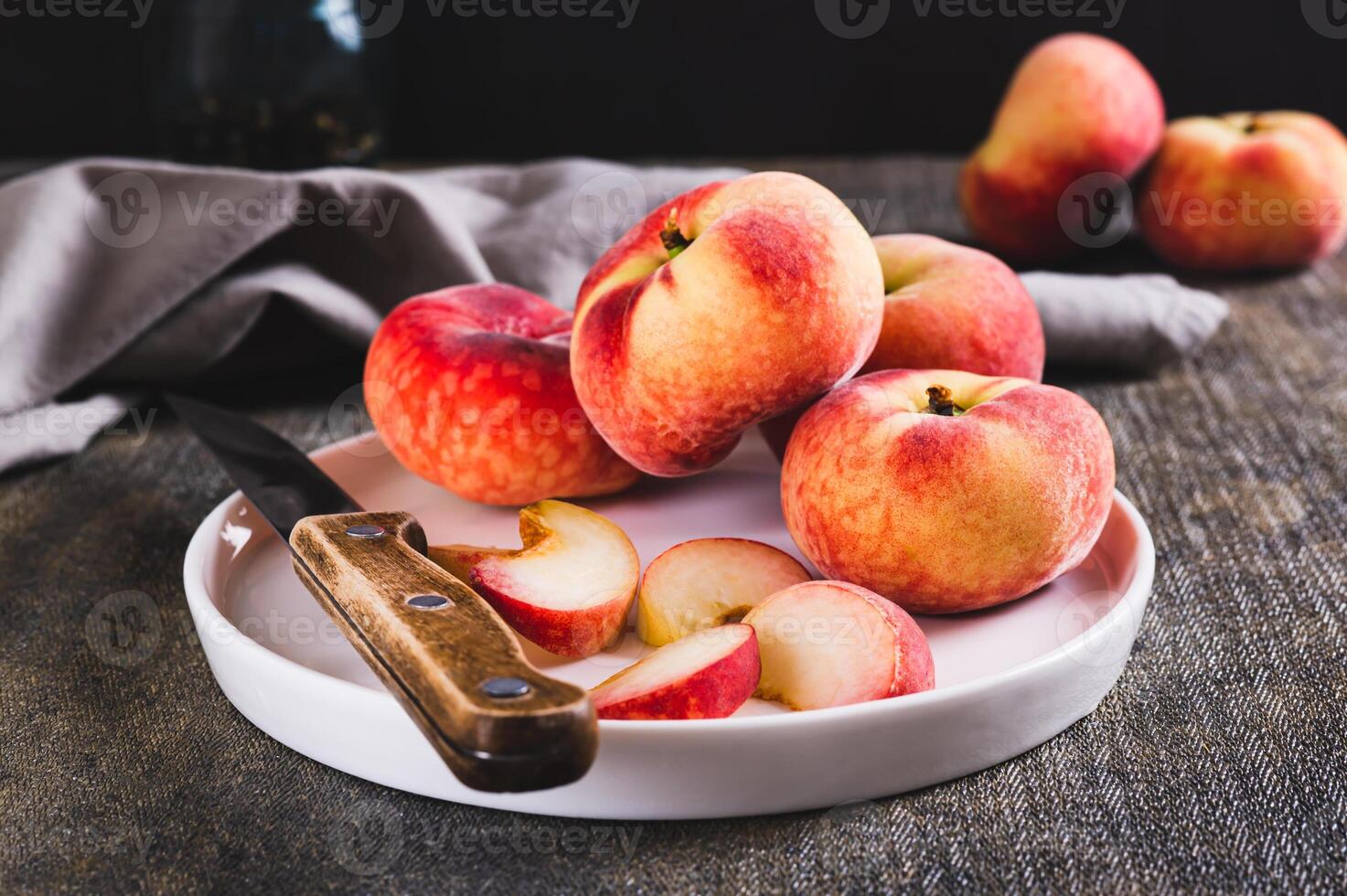 Whole and sliced peaches and a knife are placed on a plate on the table. photo