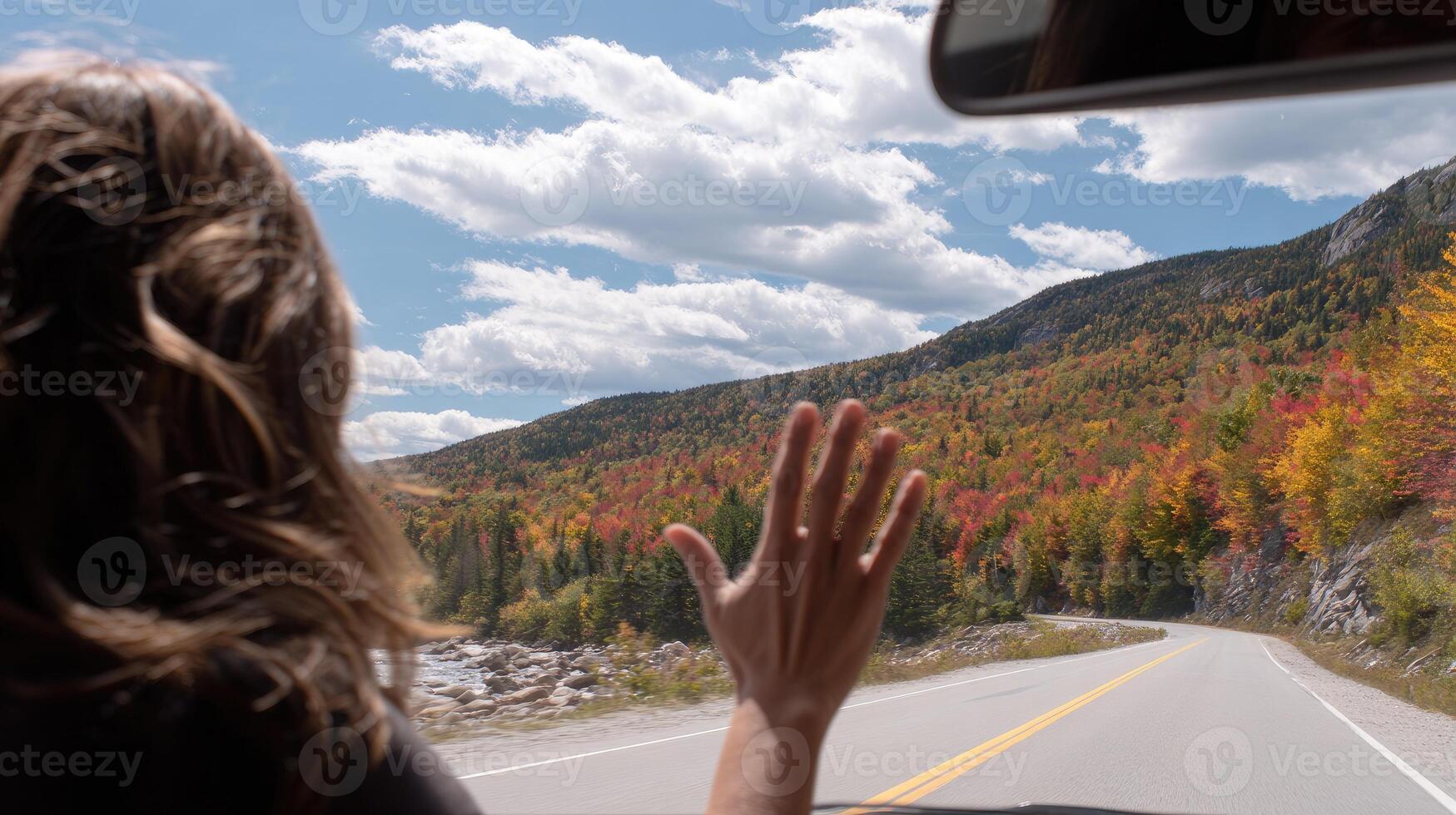 A woman driving a car on a road with autumn trees photo