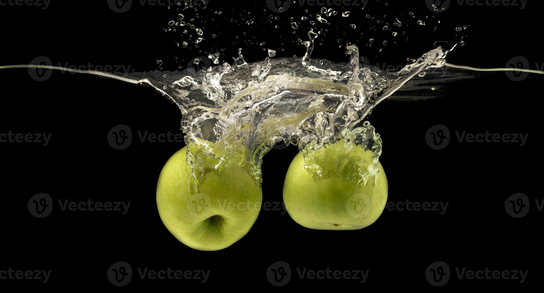 Two green apples sinking into water with air bubbles, black background photo