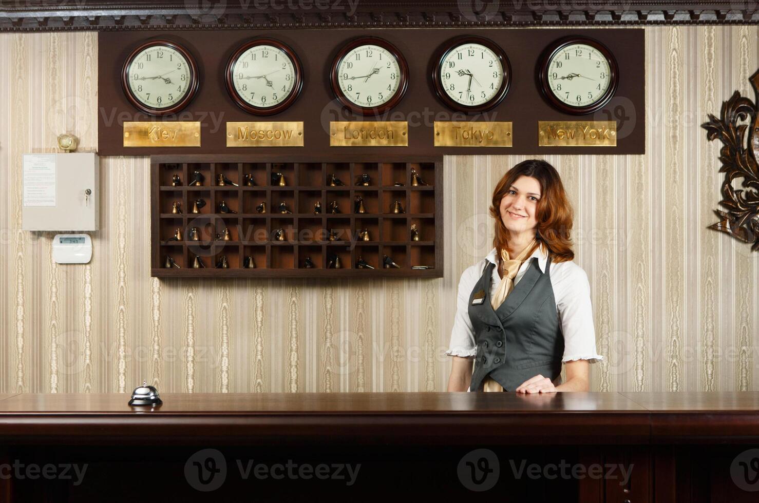 Hotel reception. Female receptionist at reception. Modern hotel reception counter desk with bell. Woman receptionist, concierge at desk. Travel, hospitality, hotel booking concept. photo