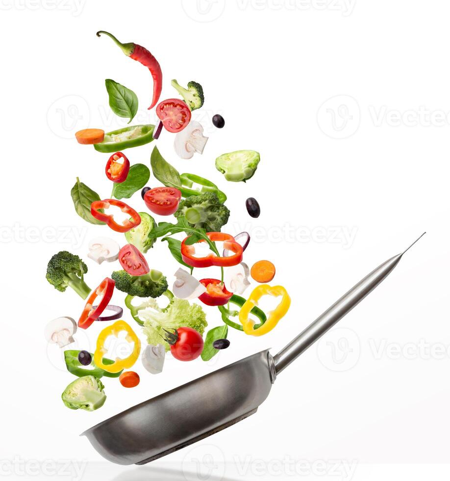 Preparing Healthy Meal. Creative collage of fresh vegetables flying into a pan, isolated on white background. Slices of tomato, lettuce, pepper and mushroom with broccoli, spinach and olives falling photo