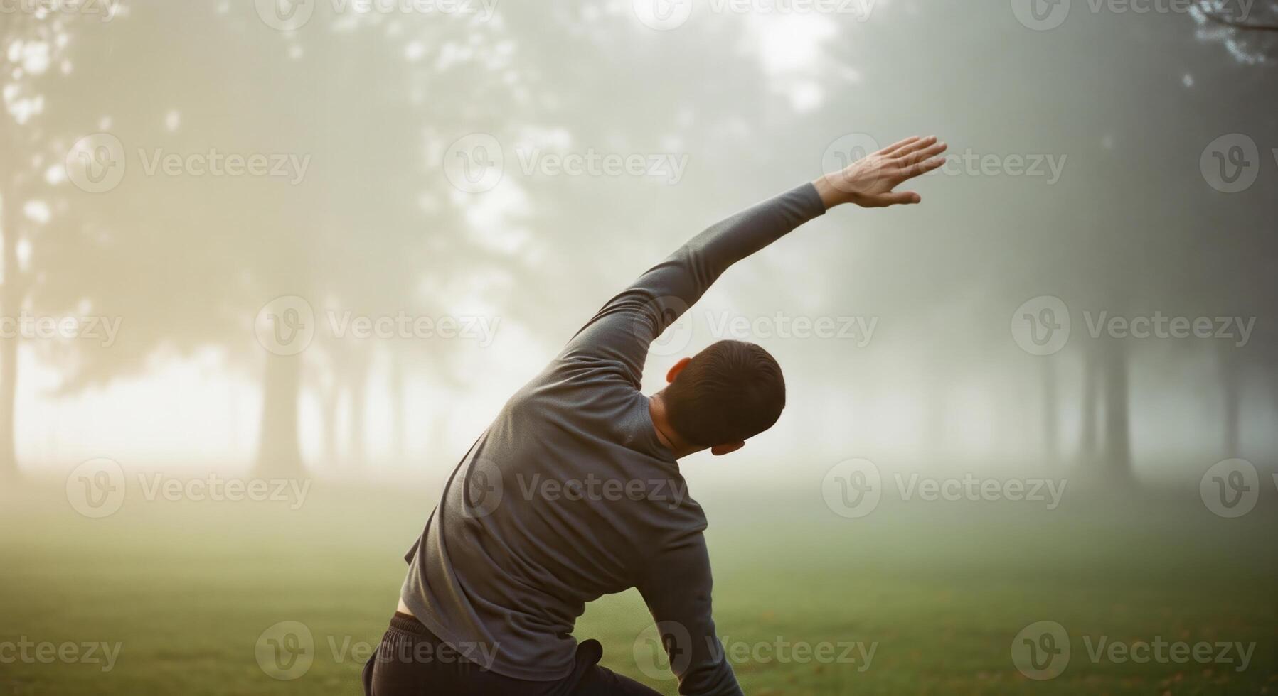 A man in a gray shirt is stretching in the grass photo
