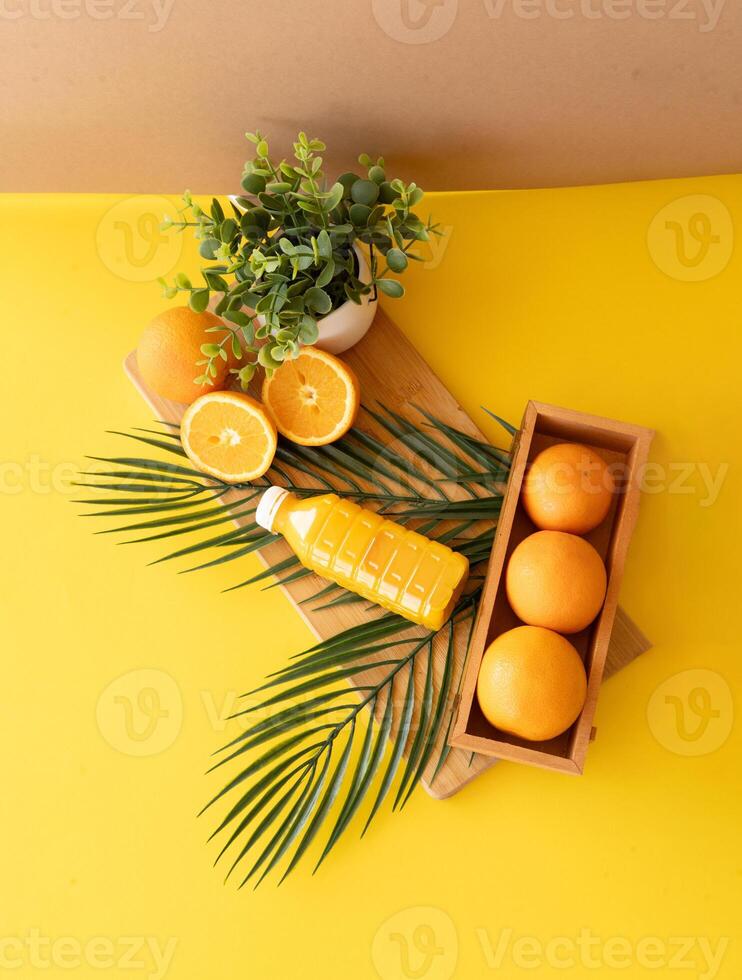 Natural wooden kitchen setup with fresh oranges and plants reflecting eco lifestyle and mindful slow living Flatlay of oranges juice bottle and green plant on wooden background with palm leaves accent photo