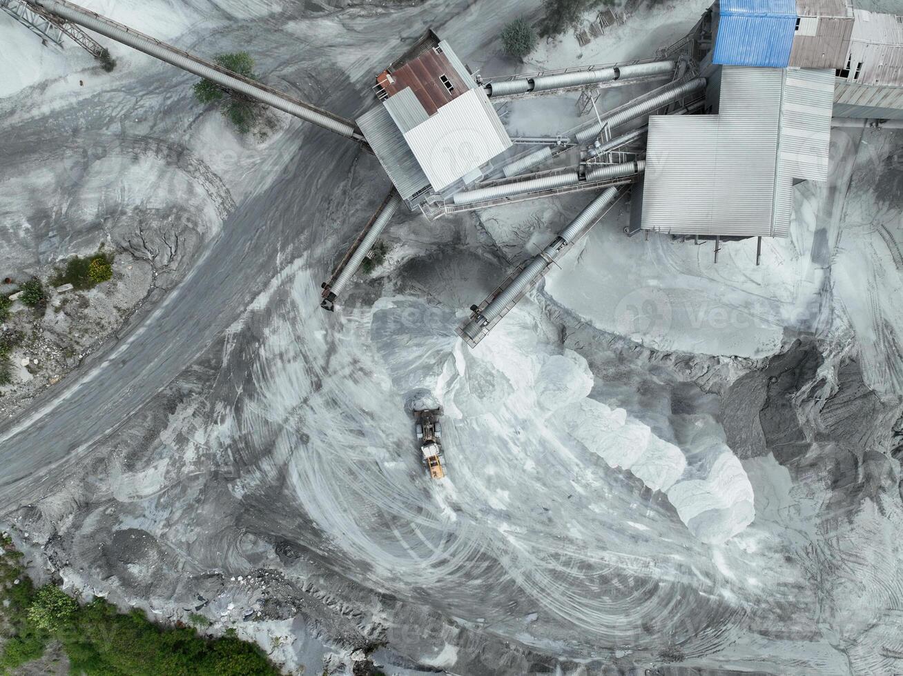 Aerial view of industrial stone crusher facility with active machinery processing raw materials in open quarry, surrounded by forest edge, highlighting environmental impact of resource extraction. photo