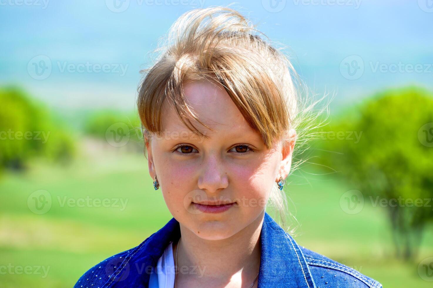 Portrait of 10 y.o. Russian smiling blonde girl on a background of green field. cute face, looking at the camera photo