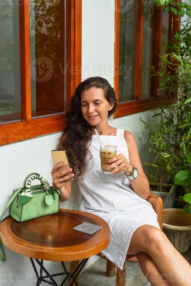 Portrait of 39 years old russian woman without make up sitting with glass of ice coffee in white dress photo