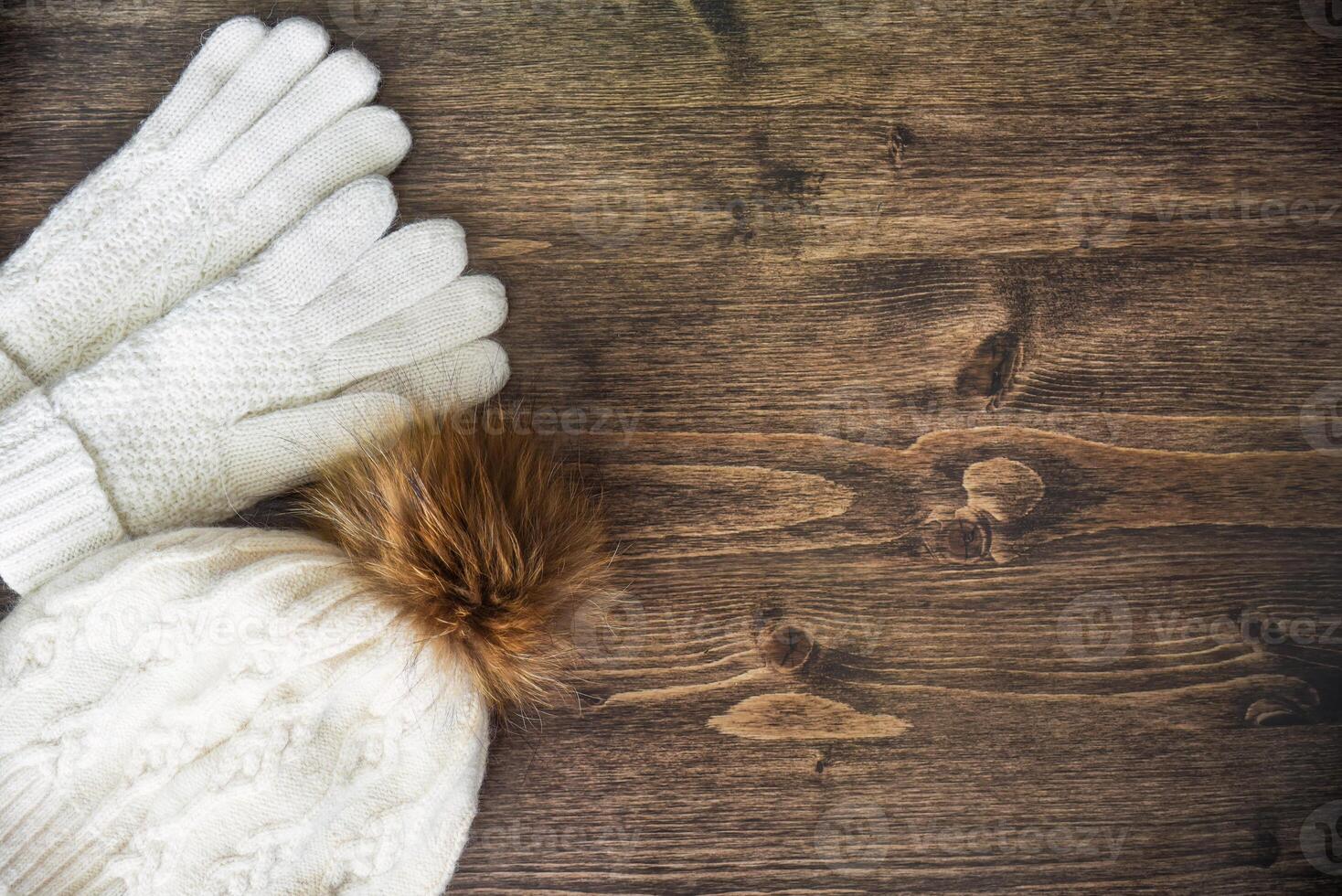 Wooden background with warm white gloves and hat with pom pom. Winter mood, copy space. photo