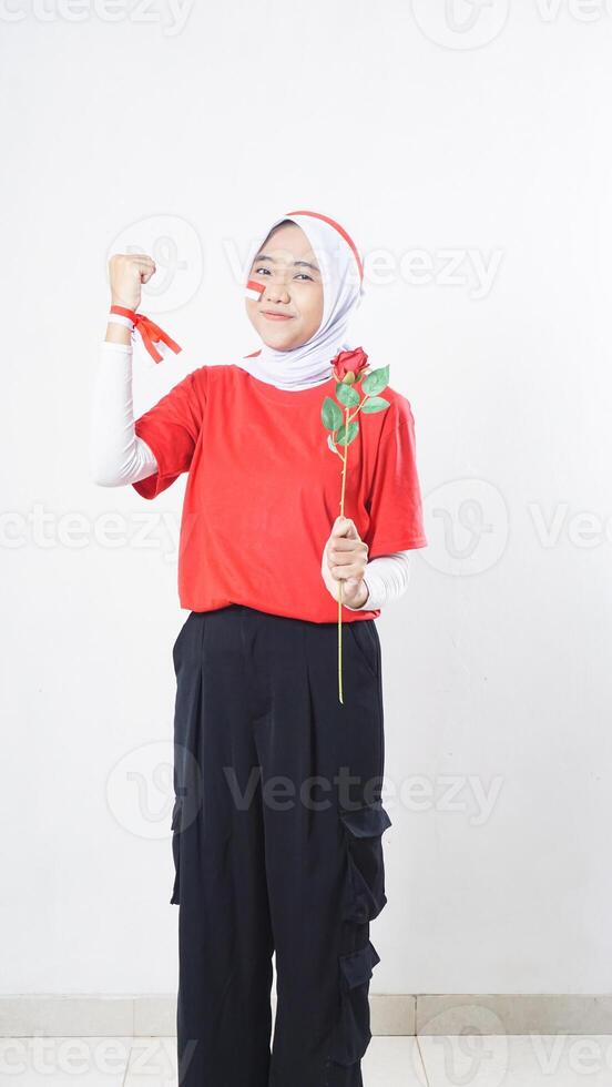 Asian girl celebrate Indonesia independence day in red and white holding a rose and raising a clenched fist isolated on white background photo