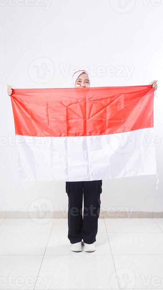 Beautiful Asian girl celebrate Indonesia independence day in red and white outfit spread Indonesian flag in front of her body isolated on white background photo