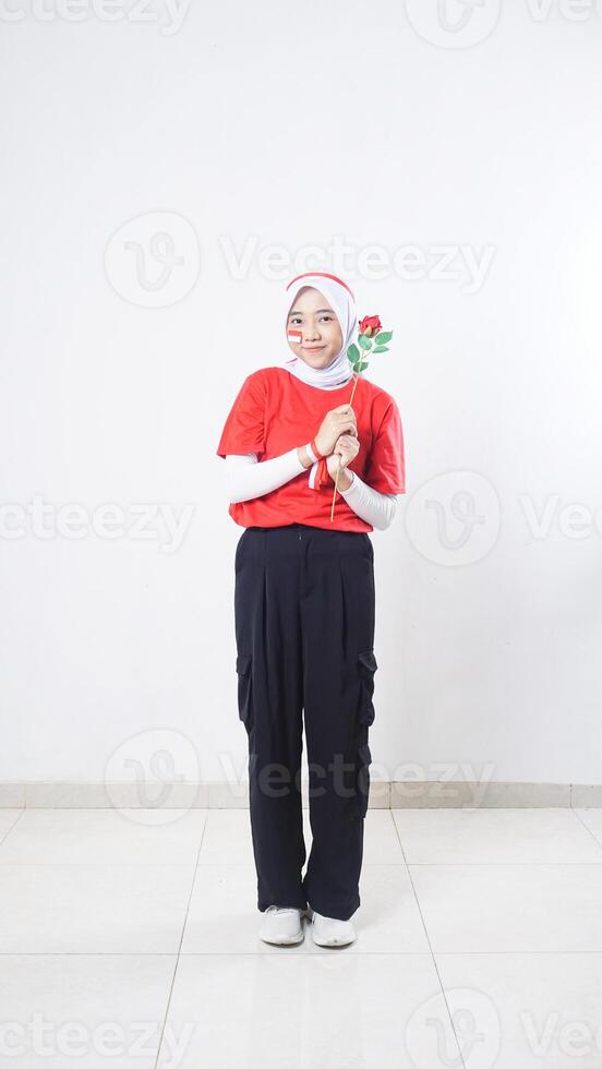 Happy Asian girl celebrate Indonesia independence day in red and white outfit holding a rose isolated on white background photo