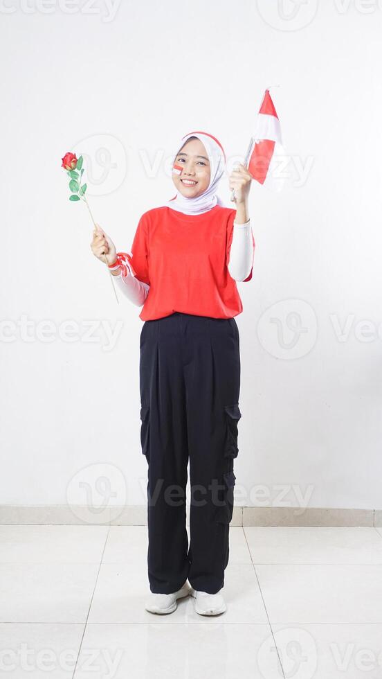 Asian girl celebrate Indonesia independence day in red and white outfit holding a rose and tiny Indonesia flag isolated on white background photo