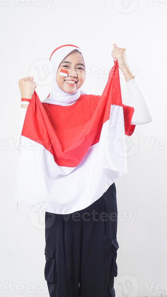 Portrait of happy Asian girl celebrate Indonesia independence day in red and white outfit holding Indonesian flag isolated on white background photo