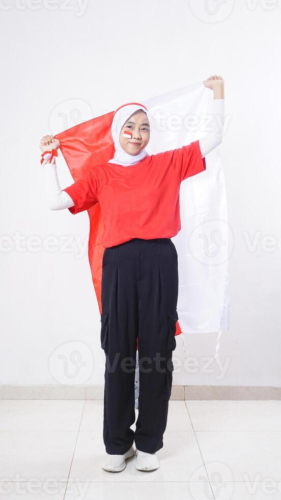 Asian girl celebrate Indonesia independence day in red and white outfit holding Indonesian flag behind her back isolated on white background photo
