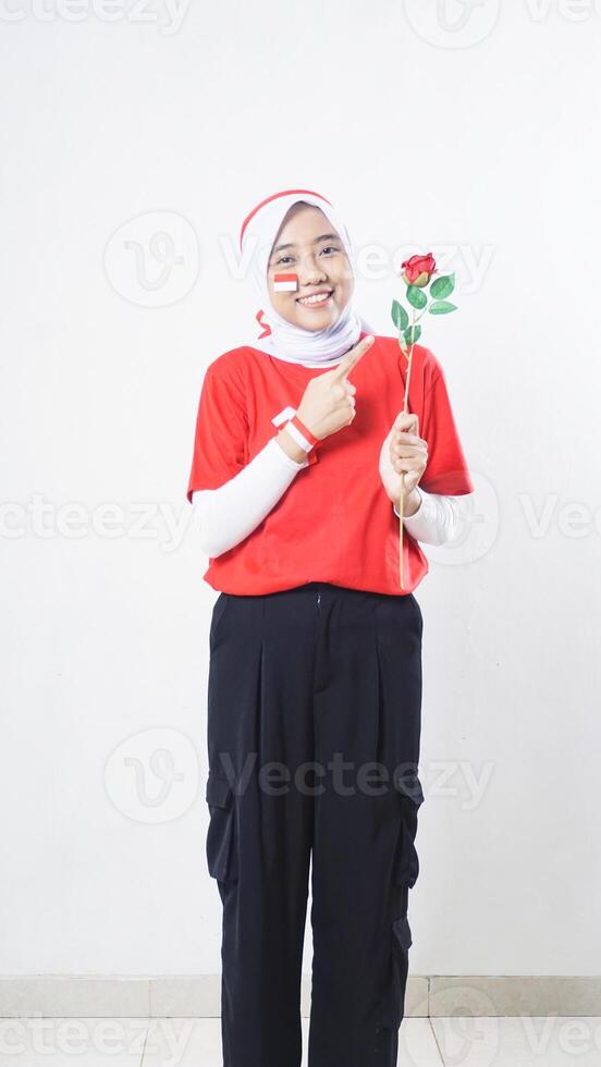 Asian girl celebrate Indonesia independence day in red and white holding and pointing at a rose isolated on white background photo